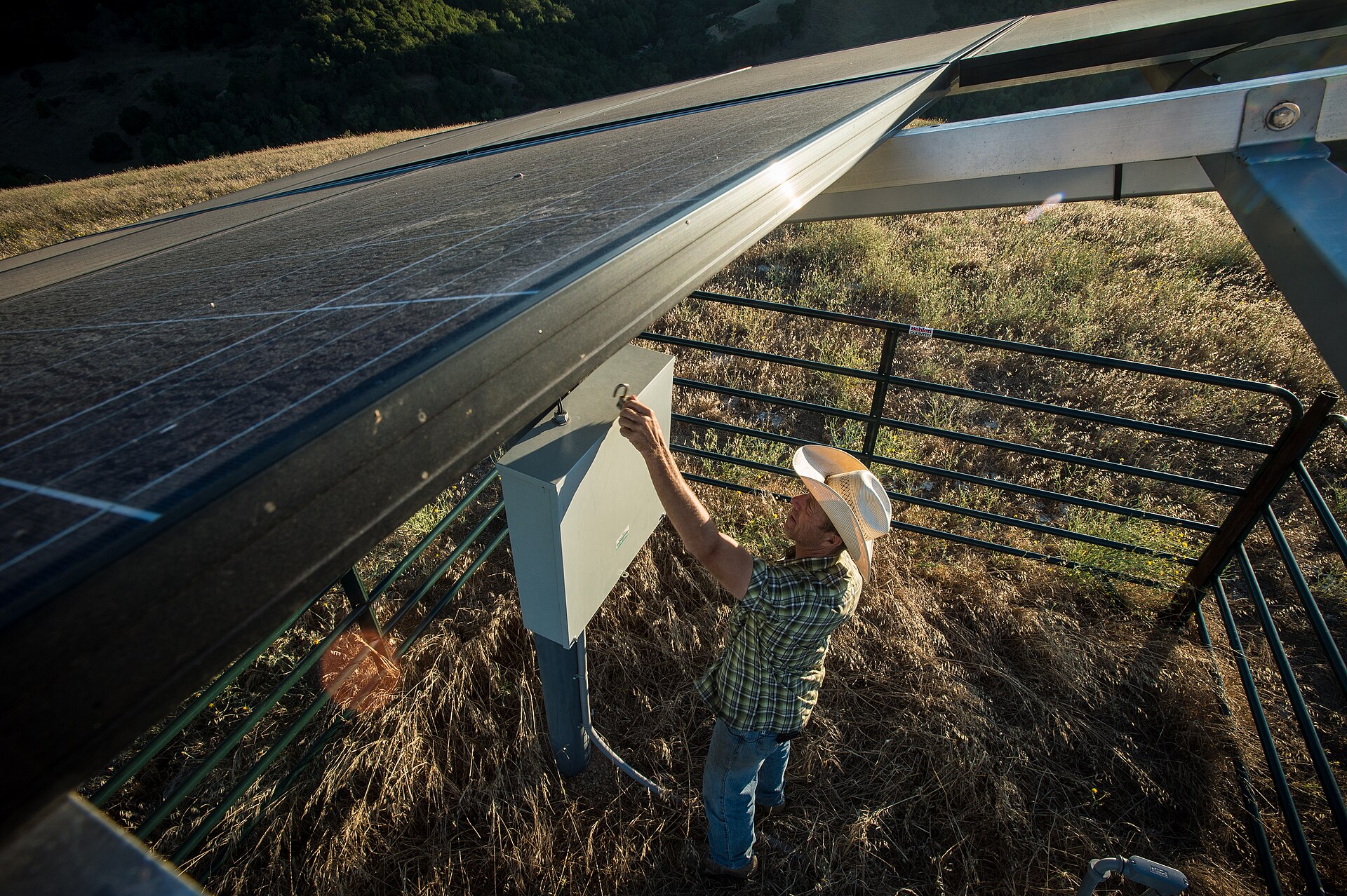 Produtor rural abrindo o quadro de controle de um sistema de bombeamento solar sob os painéis fotovoltaicos